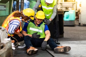man sitting down in warehouse surrounded by others wearing hi-vis vest after being injured