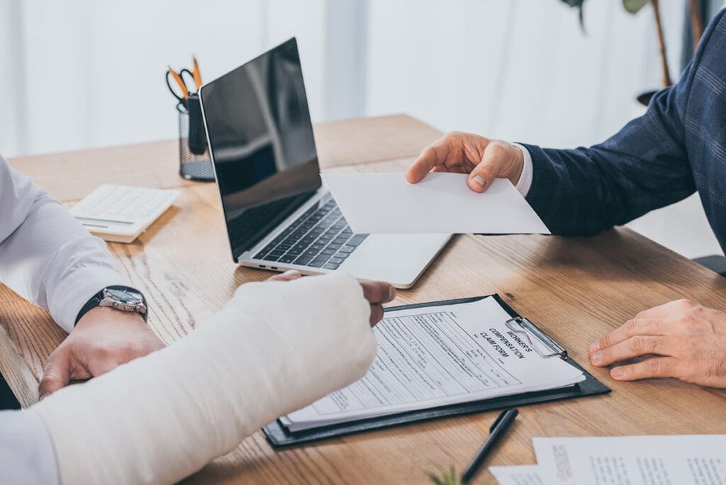 two people – one with a broken arm and one in a suit – sitting at a desk going over paperwork