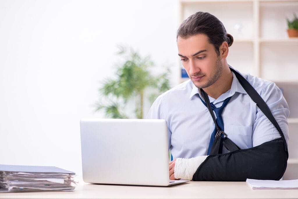 man in arm sling with ponytail working at computer