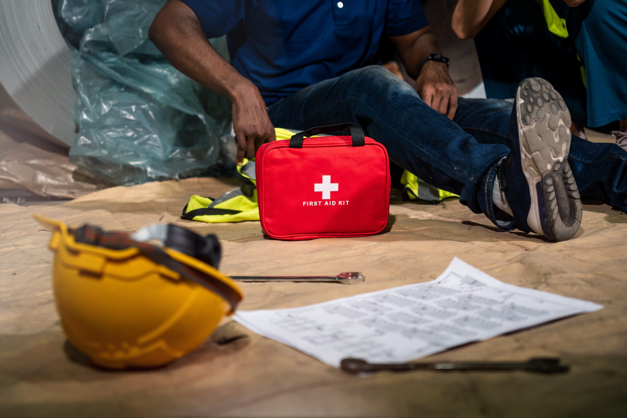 Emergency staff in safety suit use first aid kit to help a man who has an accident in factory workplace